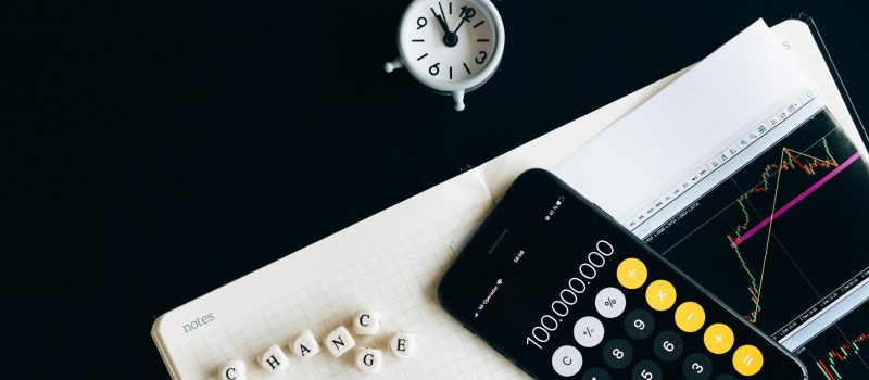 Notebook with an iPhone displaying 100,000,000, desk clock and financial charts suggesting market analysis.